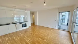 Heller offener Wohn-Essbereich mit moderner Einbauküche, Parkettboden und Zugang zum Balkon.