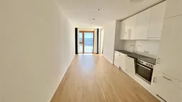 Helles Wohnzimmer mit integrierter Küchenzeile, Holzboden und Zugang zu einem Balkon.