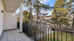 Geräumiger Balkon mit Fliesenboden und Blick ins Grüne, umgeben von Bäumen.