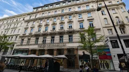 Klassisches Gebäude mit historischer Fassade und Straßencafé in einer städtischen Umgebung.