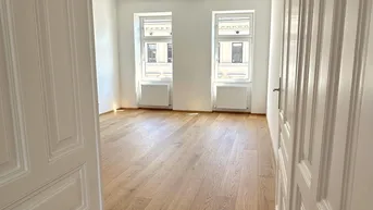 Helles Zimmer mit neuem Parkettboden und zwei Fenstern, die viel Tageslicht hereinlassen.