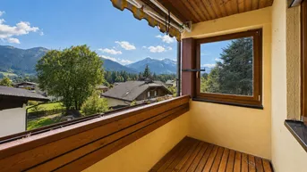 Geräumiger Balkon mit Holzboden, Markise und herrlichem Bergblick unter blauem Himmel.