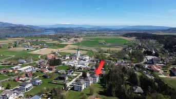 Luftaufnahme einer ländlichen Gegend mit See, Bergen und Wohngebäuden, das Objekt ist mit einem Pfeil markiert.