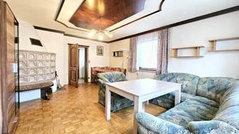 Helles Wohnzimmer mit Sitzgruppe, Parkettboden und traditionellem Kachelofen.