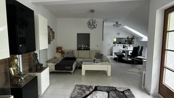 Helles, offenes Wohnzimmer mit modernen Möbeln, Fliesenboden und Blick in den Essbereich.