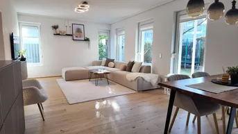 Heller offener Wohn-Essbereich mit modernem Sofa, Holzboden und großzügigem Zugang zum Garten.