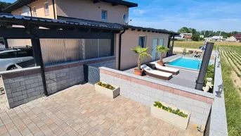 Ansicht des Hauses mit Carport, Poolbereich und Liegestühlen, umgeben von Feldern.