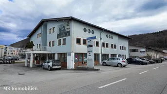 Mehrstöckiges Geschäftsgebäude mit Parkplätzen und umliegender Landschaft unter bewölktem Himmel.