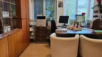 Helles Büro mit mehreren Arbeitsplätzen, Holzschränken und Blick ins Grüne durch die Fenster.