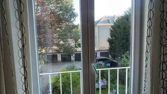 Französischer Balkon mit Blick auf den grünen Garten und die umliegenden Gebäude.