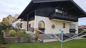 Traditionelles Haus mit Balkon, Garten und Wäschespinne unter bewölktem Himmel.
