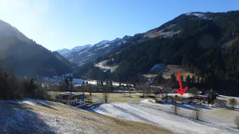 Weitläufige Ansicht eines verschneiten Tals mit Bergen und vereinzelten Häusern unter blauem Himmel.