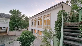 Seitenansicht des Wohngebäudes mit Außentreppe und üppiger Vegetation im Gartenbereich.