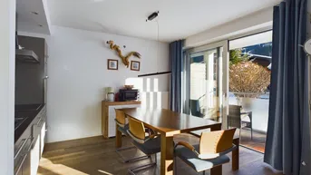 Helles Esszimmer mit Holztisch, modernen Stühlen und Zugang zum Balkon, kombiniert mit Küchenzeile.
