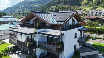 Modernes Mehrfamilienhaus mit Balkonen, Solaranlage und Bergblick in grüner Umgebung.
