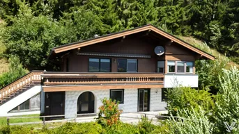 Traditionelles Holzhaus in alpiner Umgebung mit Satteldach und Balkon.