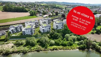 Luftaufnahme moderner Wohngebäude mit Gründächern und Photovoltaikanlagen, umgeben von Natur und Wasser.