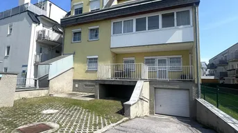 Gelbes Mehrfamilienhaus mit Garage, Balkon und Zufahrt unter blauem Himmel.