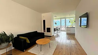 Gemütliches Wohnzimmer mit schwarzem Sofa, modernem Kamin und Holzboden mit Bergblick.