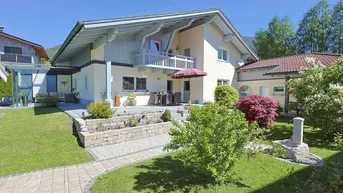 Großzügiges Einfamilienhaus mit gepflegtem Garten, Terrasse und Balkon, umgeben von grüner Landschaft.