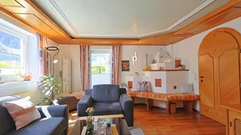Gemütliches Wohnzimmer im alpinen Stil mit Holzbalkendecke, Kachelofen und Parkettboden.