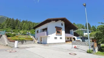 Freistehendes Haus mit weißer Fassade, Holzelementen und Balkonen in alpiner Umgebung.