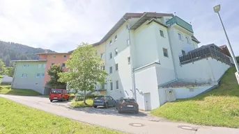 Mehrstöckiges Wohngebäude mit mehreren Balkonen und Parkplätzen in ländlicher Umgebung.