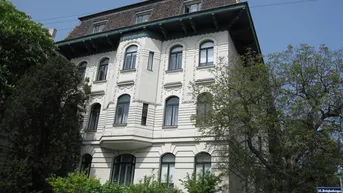 Klassisches Mehrfamilienhaus mit historischer Fassade, Mansarddach und grüner Umgebung.