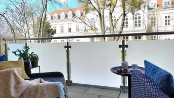 Möblierter Balkon mit Steinboden und Blick auf gegenüberliegende Gebäude und Bäume.