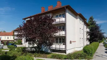 Mehrfamilienhaus mit mehreren Balkonen und gepflegter Grünanlage unter blauem Himmel.