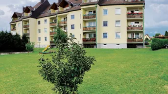 Mehrfamilienhaus mit mehreren Balkonen, umgeben von einer gepflegten Grünfläche und einem kleinen Spielplatz.