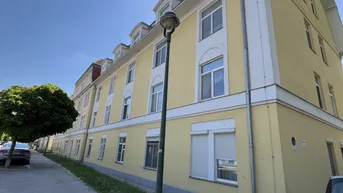 Gelbe Fassade eines Mehrfamilienhauses mit vielen Fenstern und einem Gehweg davor.