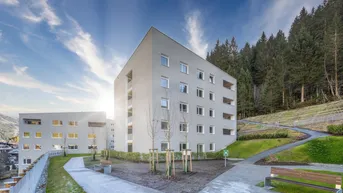Moderne Wohngebäude mit schlichter Fassade, umgeben von grüner Natur und angelegten Wegen.