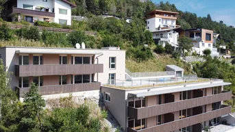 Mehrere moderne Gebäude an einem Hang mit Balkonen und begrünten Dächern, umgeben von Bäumen.