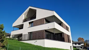 Modernes Mehrfamilienhaus mit weißer Fassade, Holzdetails und Balkonen unter blauem Himmel.