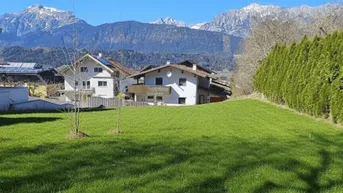 Grüne Wiese mit Blick auf die umliegenden Berge und Wohnhäuser in sonniger Lage.