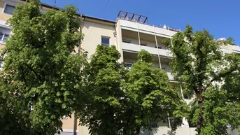 Mehrstöckiges Wohngebäude mit Balkonen und üppigem Grün im Vordergrund unter blauem Himmel.