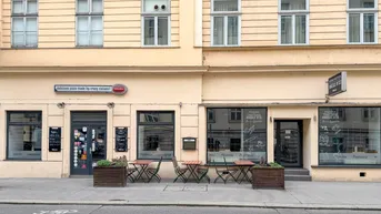 Fassade eines Gebäudes mit Restaurants im Erdgeschoss und Fenstern im Obergeschoss, inklusive Außensitzplätzen auf dem Bürgersteig.