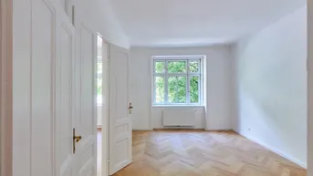 Geräumiges Zimmer mit klassischem Fischgrätparkett und großen Fenstern, die eine helle Atmosphäre schaffen.