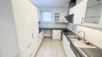 Funktionale Küche mit weißen Schränken, dunklen Arbeitsplatten und Fliesenboden.