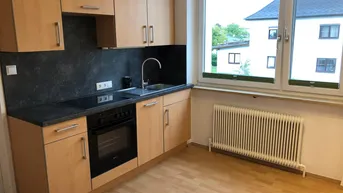 Helle Küche mit Holzschränken, dunkler Arbeitsplatte, integriertem Herd und Blick ins Grüne.