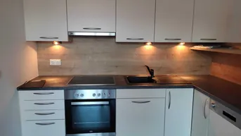 Moderne Einbauküche mit weißen Schränken, dunkler Arbeitsplatte und integrierten Geräten.