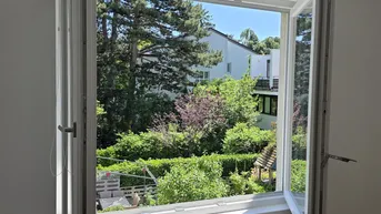 Offenes Fenster mit Blick auf einen grünen Garten und umliegende Häuser an einem sonnigen Tag.