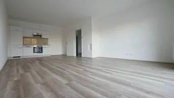 Helles, offenes Wohnzimmer mit integrierter Küchenzeile und modernem Laminatboden.