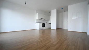 Heller, offener Wohnbereich mit integrierter Küche und modernem Laminatboden in einem Neubau.
