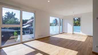 Helles, leeres Wohnzimmer mit großen Fenstern, Holzboden und Zugang zu einem Balkon.