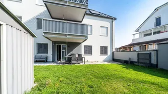 Hinterhof mit Rasenfläche, möblierter Terrasse und Balkonen an der Fassade eines Neubaus.