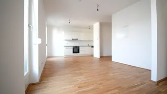Heller offener Wohnbereich mit integrierter Küche und modernem Parkettboden, ideal für geselliges Beisammensein.