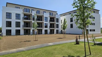 Moderne Wohngebäude mit weißer Fassade und gepflegter Grünfläche im Außenbereich unter blauem Himmel.