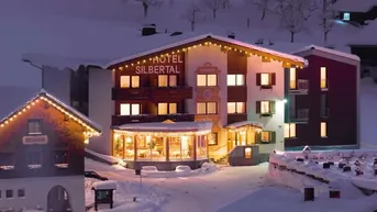 Beleuchtetes Hotel Silberthal in verschneiter Winterlandschaft bei Nacht, festlich geschmückt mit Lichterketten.